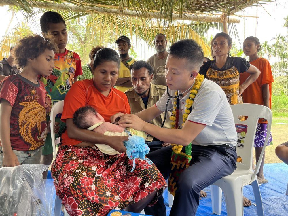 2023年8月5日，在巴布亞新幾內(nèi)亞中央省的一個(gè)村莊里，第12批援巴新中國(guó)醫(yī)療隊(duì)副隊(duì)長(zhǎng)、新生兒科副主任醫(yī)師劉振球?yàn)閶雰禾?lè)聽診檢查。泰樂(lè)出生時(shí)患有重癥，一度生命垂危，經(jīng)過(guò)劉振球與當(dāng)?shù)蒯t(yī)護(hù)人員的救治最終痊愈。從2002年起，中國(guó)連續(xù)向巴新派出12批醫(yī)療隊(duì)，為提高巴新醫(yī)療衛(wèi)生水平作出積極貢獻(xiàn)。