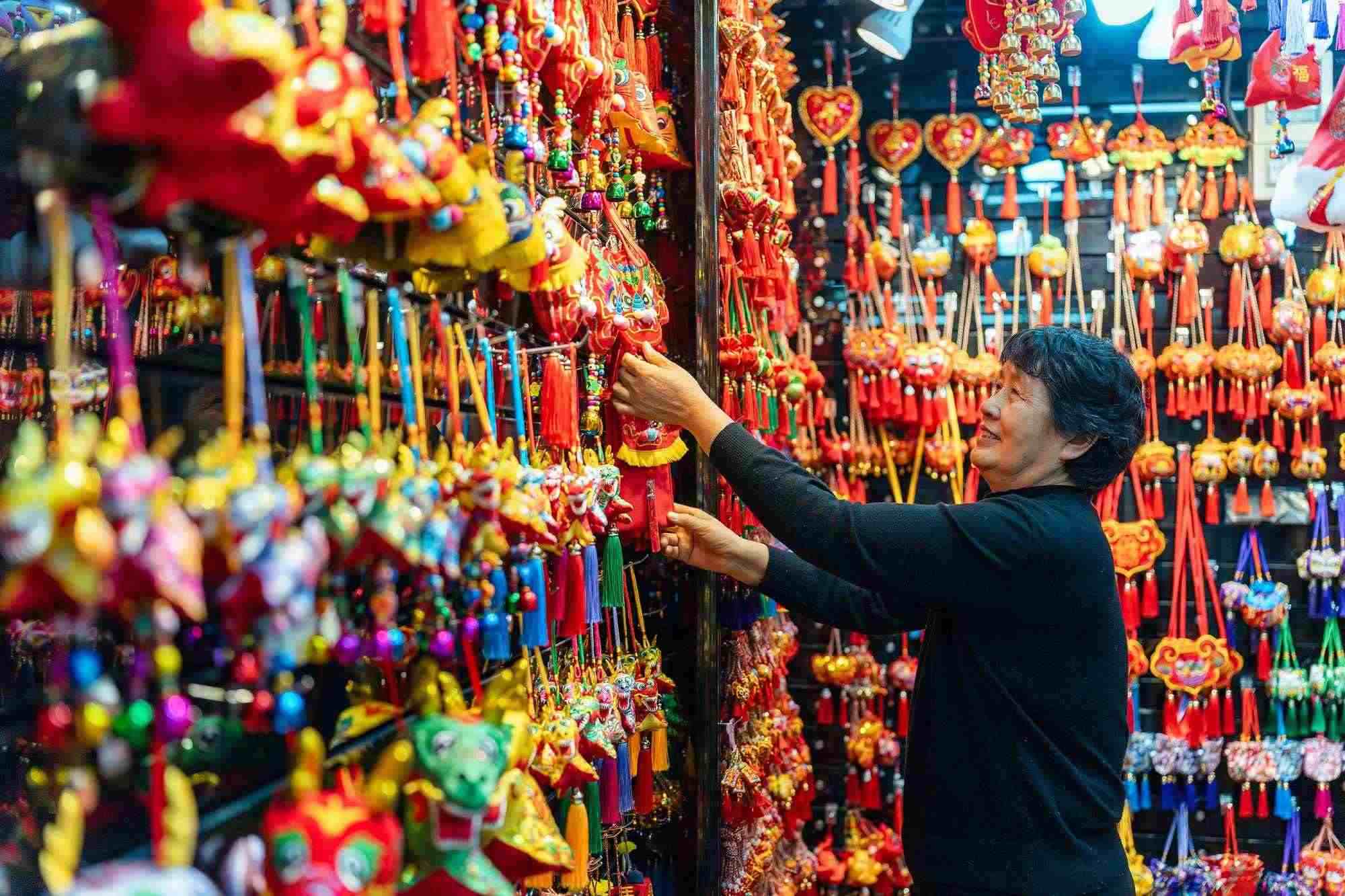 2023年12月11日，金華義烏國際商貿(mào)城，龍年喜慶用品掛滿攤位，顧客正在挑選中。