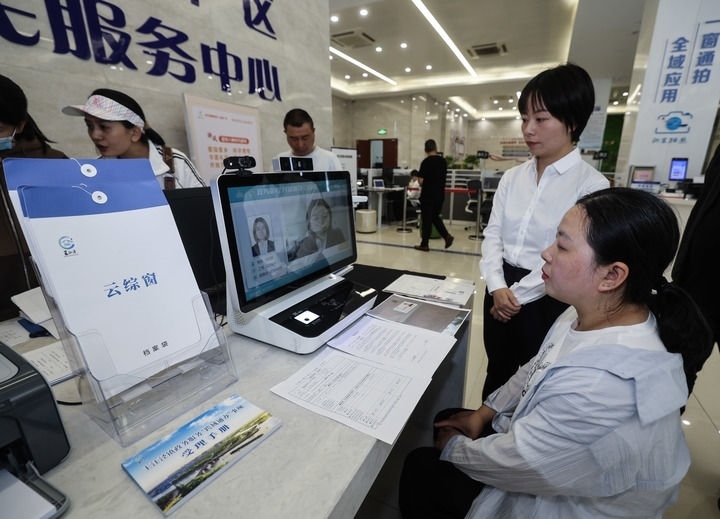 在浙江省嘉興市秀洲區(qū)王江涇鎮(zhèn)便民服務中心的“跨域通辦·云綜窗”窗口，辦理開業(yè)登記的個體工商戶（右一）通過該系統(tǒng)與江蘇省蘇州市吳江區(qū)盛澤鎮(zhèn)行政審批局工作人員視頻連線，進行身份讀取及材料線上審核（2024年5月9日攝）。新華社記者 徐昱 攝