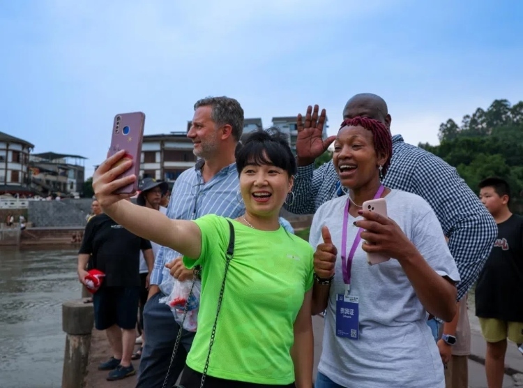 2024“一帶一路”媒體合作論壇聯(lián)合采訪調(diào)研行成員在樂山蘇稽古鎮(zhèn)與游客合影留念。本報記者 伊霄攝